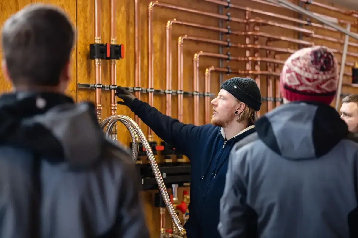 Heizungsmonteur erklärt Auszubildenden die Kupferrohr-Installation an einer Heizungsanlage