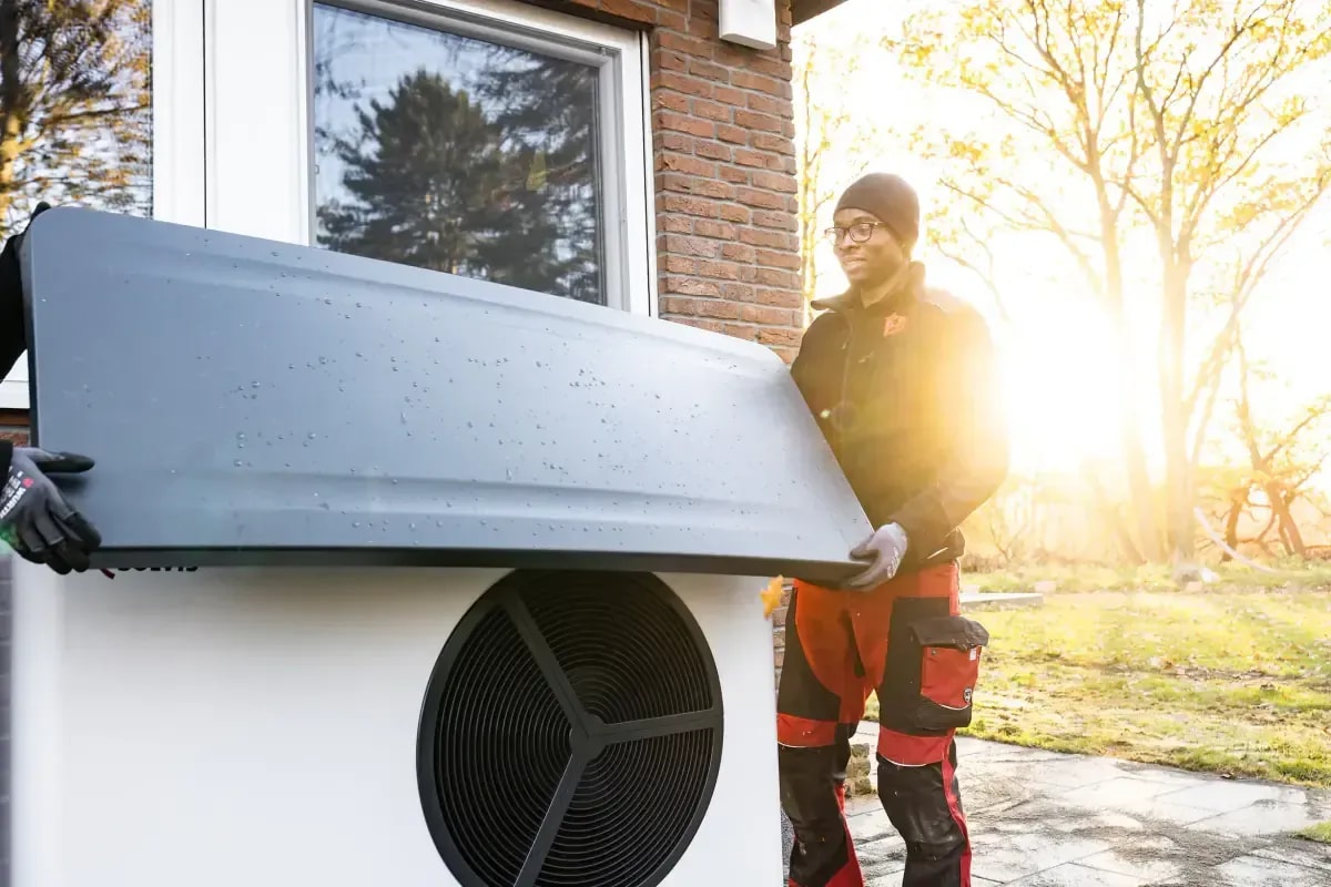 Techniker installiert eine moderne Luft-Wärmepumpe vor einem Wohnhaus im Sonnenlicht
